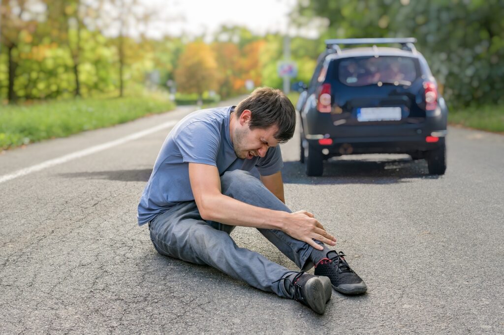 photo of an Injured man on road in front of a car.