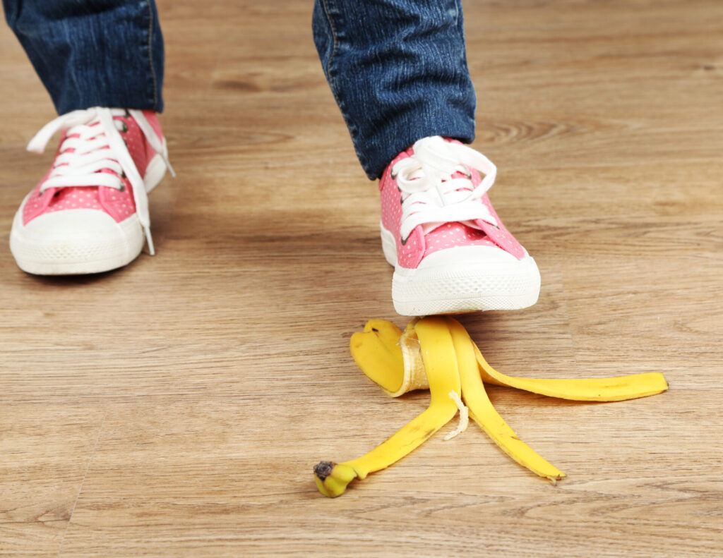 Person in pink sneakers about to step on a banana peel on a wooden floor